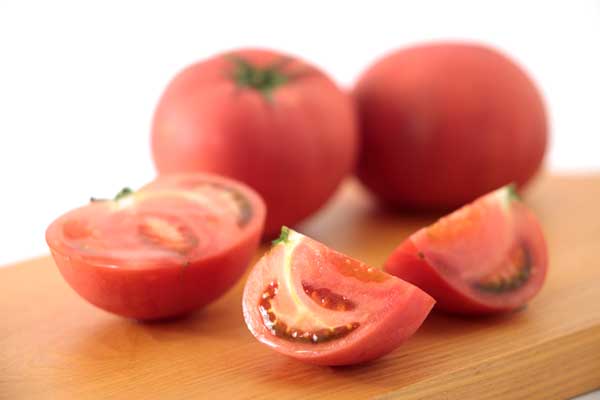 まな板の上、手前に4分の1に切ったトマト2切れ置いて、背後に2個と半分に切ったトマトを置いた写真