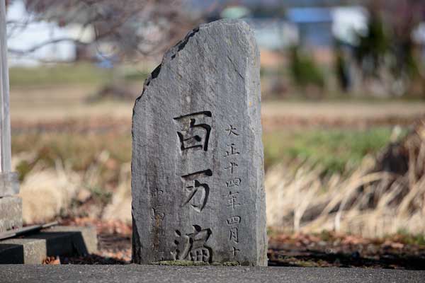 小春日和の長閑な村外れに設置されている古びた百万遍の石碑。