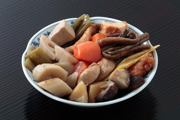 青森県津軽地方の煮しめ。山菜、野菜、ちくわ、椎茸、魚などを一緒に煮た料理。正月などに食べられる。皿に盛りつけた煮しめを黒っぽいお盆のバックで撮影1カット