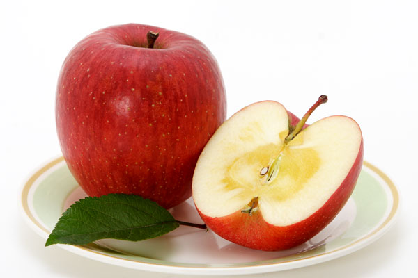 一個のりんごと半分にカットして蜜が入った断面を見せた写真。白い背景、皿の上、りんごの葉を一枚、イメージ画像、サンフジ